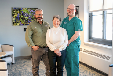 Fontaine Melus stands smiling between two members of the Mobile Integrated Healthcare team from Monadnock Community Hospital. On the left is Dr. Lucas Shippee in a green shirt, and on the right is paramedic Joshua Patrick in green scrubs.
