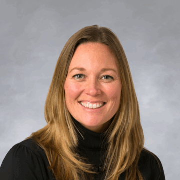 Smiling woman with long, light brown hair, wearing a black turtleneck, photographed against a white background.