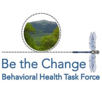 A circular image of a green, tree-covered mountain is positioned at the top center of the graphic. Below, the text 'Be the Change' is written in blue, with the words 'Behavioral Health Task Force' underneath. A blue dragonfly is featured on the right side of the image, aligned with the text