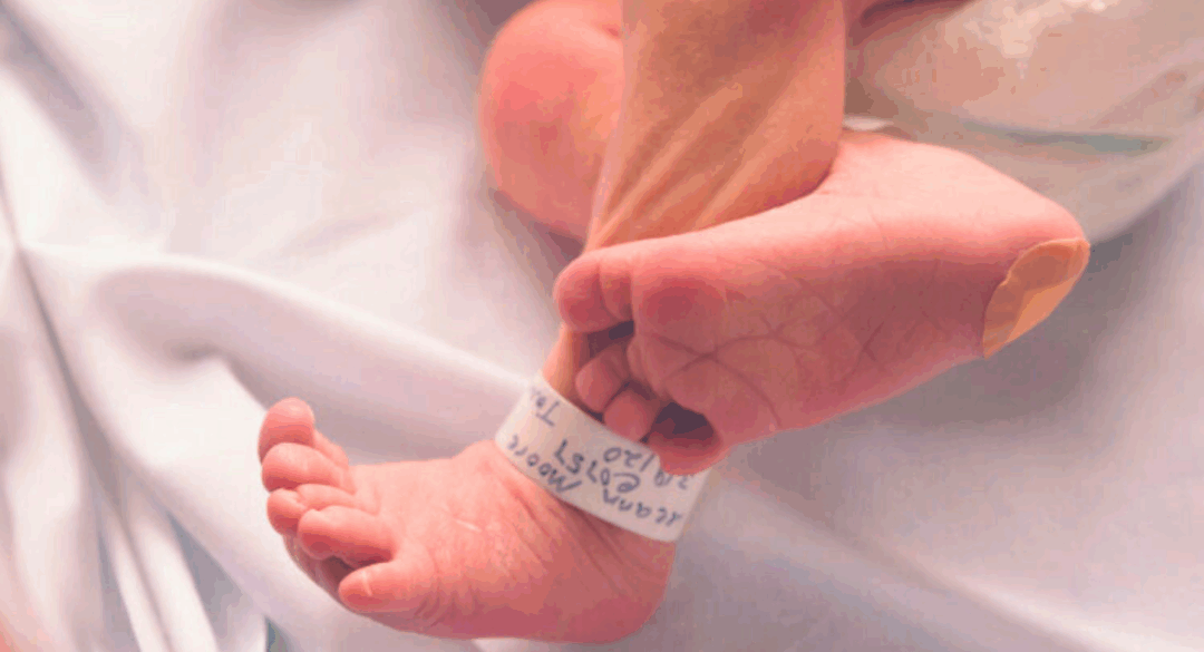 Close-up of a newborn’s tiny feet with a hospital ID band wrapped around the ankle