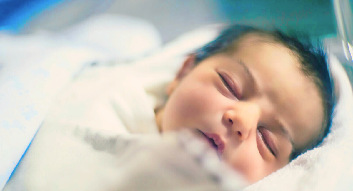 Close-up of a newborn baby with dark hair peacefully sleeping in a hospital blanket
