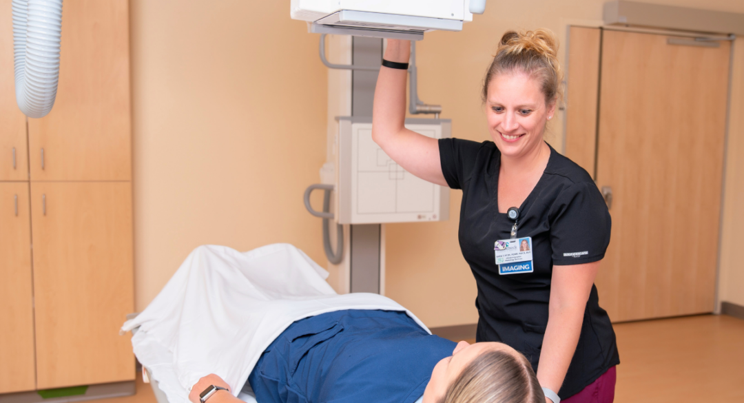 A radiology technician smiles warmly while preparing an ultrasound machine for a patient lying on the table, showcasing compassionate and skilled healthcare service