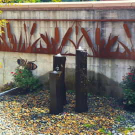 View of the Deb Cilley and Family Healing Garden at Monadnock Community Hospital featuring a fountain, natural landscaping, bee murals by artist Matt Willey, and a custom metal sculpture inspired by native plants. The peaceful outdoor space can be seen from the Oncology Suite and provides a calming view for patients, families, and staff.