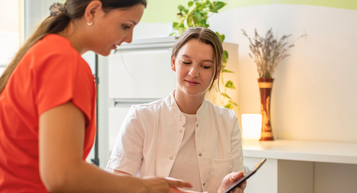 Healthcare provider in a white coat reviewing a tablet with a patient in a warmly lit clinic office with plants and soft lighting.