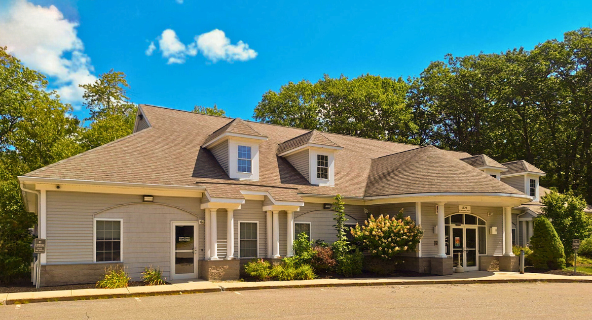 Front entrance of New Ipswich Family Medicine, a primary care clinic in New Ipswich NH, showing the building’s doorway with columns, windows, and surrounding landscaping under a sunny sky.