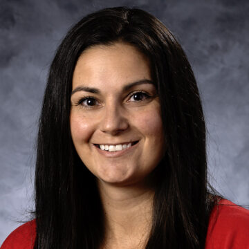 A professional portrait of Chelsie Fukuda, a physical therapist with long, straight, dark brown hair, smiling warmly. She is wearing a bright red top against a soft, neutral-colored background.