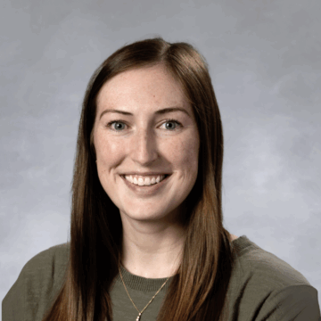 A professional portrait of Morgan Jenkins, an occupational therapist with long, straight brown hair, smiling brightly. She is dressed in a professional top and stands against a neutral background.