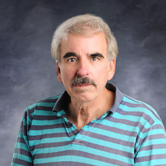 Portrait of Dr. Eric M. Bonnem, a board-certified medical oncologist at Monadnock Community Hospital. He has light gray hair, a mustache, and is wearing a teal and navy striped polo shirt, photographed against a dark gray studio background.