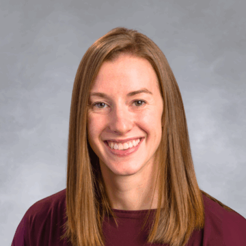 Smiling woman with straight, shoulder-length light brown hair, wearing a maroon top, in front of a soft gray studio background.