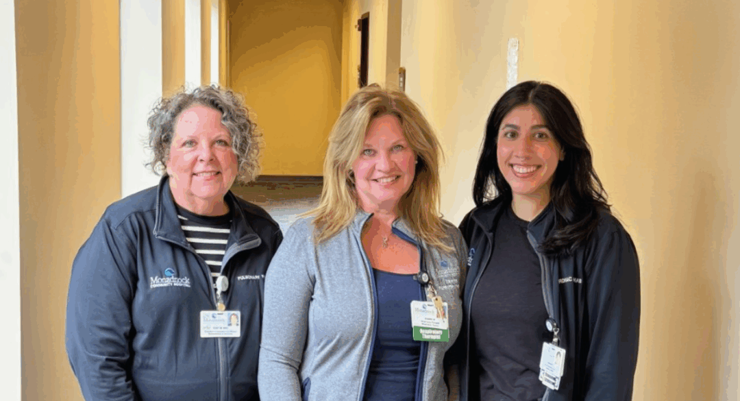 Three Monadnock Community Hospital staff members stand together smiling in a hallway. All are wearing MCH jackets and ID badges, with the middle staff member’s badge identifying her as a respiratory therapist.