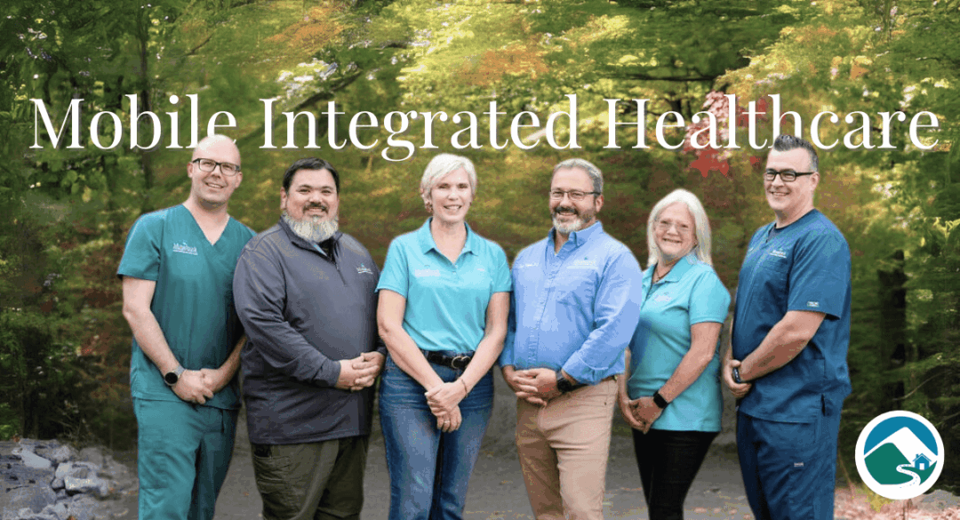 Group photo of the Mobile Integrated Health team at Monadnock Community Hospital, standing outdoors with a lush, green forest background. Team members are dressed in professional attire, smiling warmly to the camera, creating a welcoming and approachable impression