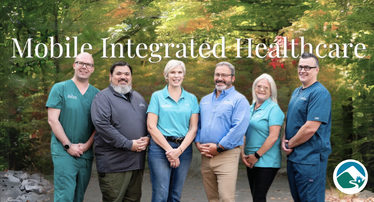 Group photo of the Mobile Integrated Health team at Monadnock Community Hospital, standing outdoors with a lush, green forest background. Team members are dressed in professional attire, smiling warmly to the camera, creating a welcoming and approachable impression