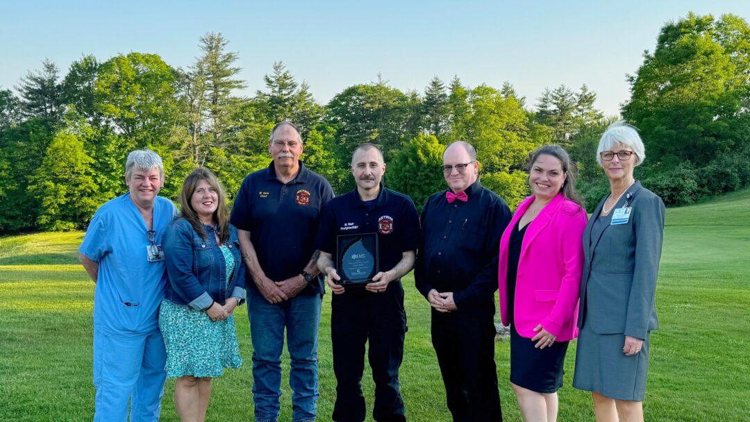 EMS Achievement recipient Matt Mair alongside Antrim Fire Department’s Chief and Deputy Chief and MCH leaders. A group of seven people, including EMS workers and hospital staff, standing outdoors on a grassy area, smiling at the camera. One person is holding an award plaque