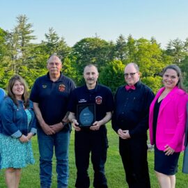 EMS Achievement recipient Matt Mair alongside Antrim Fire Department’s Chief and Deputy Chief and MCH leaders. A group of seven people, including EMS workers and hospital staff, standing outdoors on a grassy area, smiling at the camera. One person is holding an award plaque