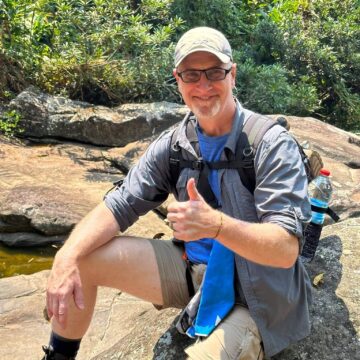 Dr Harrington sits on a big rock with a thumbs up 