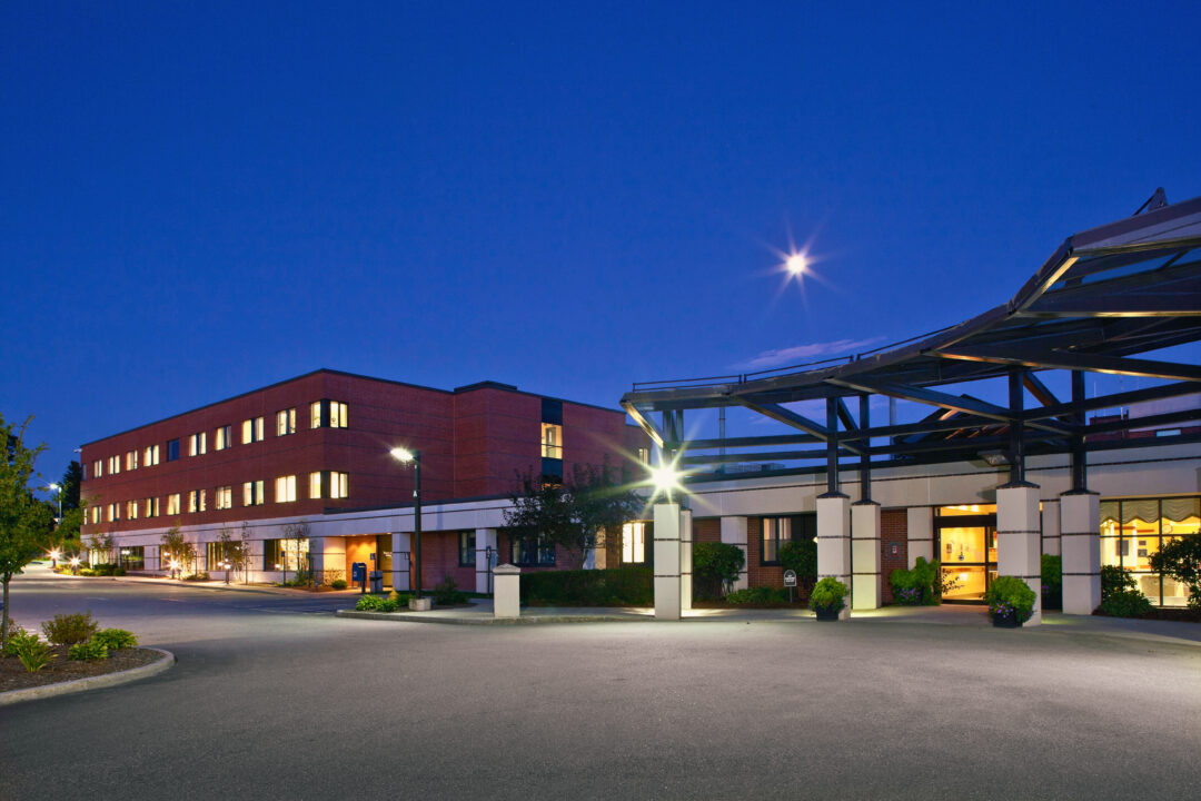 Monadnock Community Hospital main entrance at night, with the building and parking area illuminated, and a clear night sky with the moon visible
