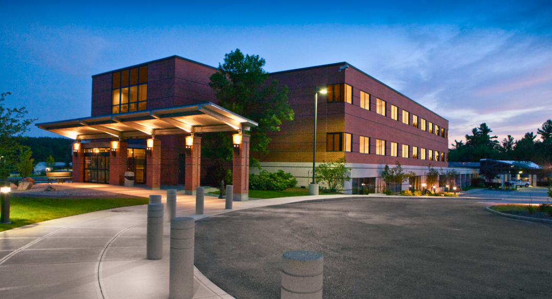 Monadnock Community Hospital's Medical Arts Building at dusk, with warm lights illuminating the entrance and the surrounding area