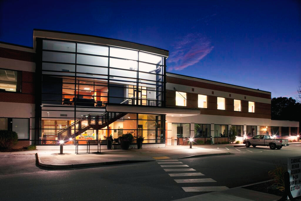Monadnock Community Hospital's Wellness Center at night, featuring large glass windows and modern architectural design, with the building brightly lit from within