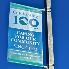 A colorful banner against a bright blue sky, celebrating Monadnock Community Hospital's 100th anniversary with the slogan "Caring for Our Community Since 1923."