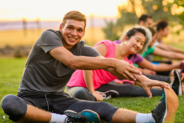 People stretching outdoors in a fitness class on a grassy field, smiling and enjoying the activity together at sunset