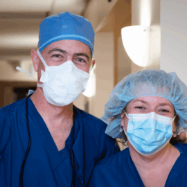 Two medical professionals in blue scrubs and surgical masks, smiling at the camera inside Monadnock Community Hospital.