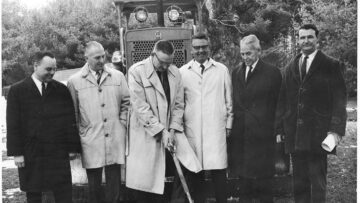 A historical black-and-white photo of six men in coats standing in front of construction equipment, participating in a groundbreaking ceremony for Monadnock Community Hospital.