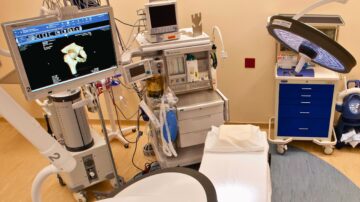 A color photograph of an operating room featuring a large monitor displaying medical imaging, along with various surgical equipment and instruments. The room is ready for a surgical procedure, reflecting the advanced technology used in modern healthcare.