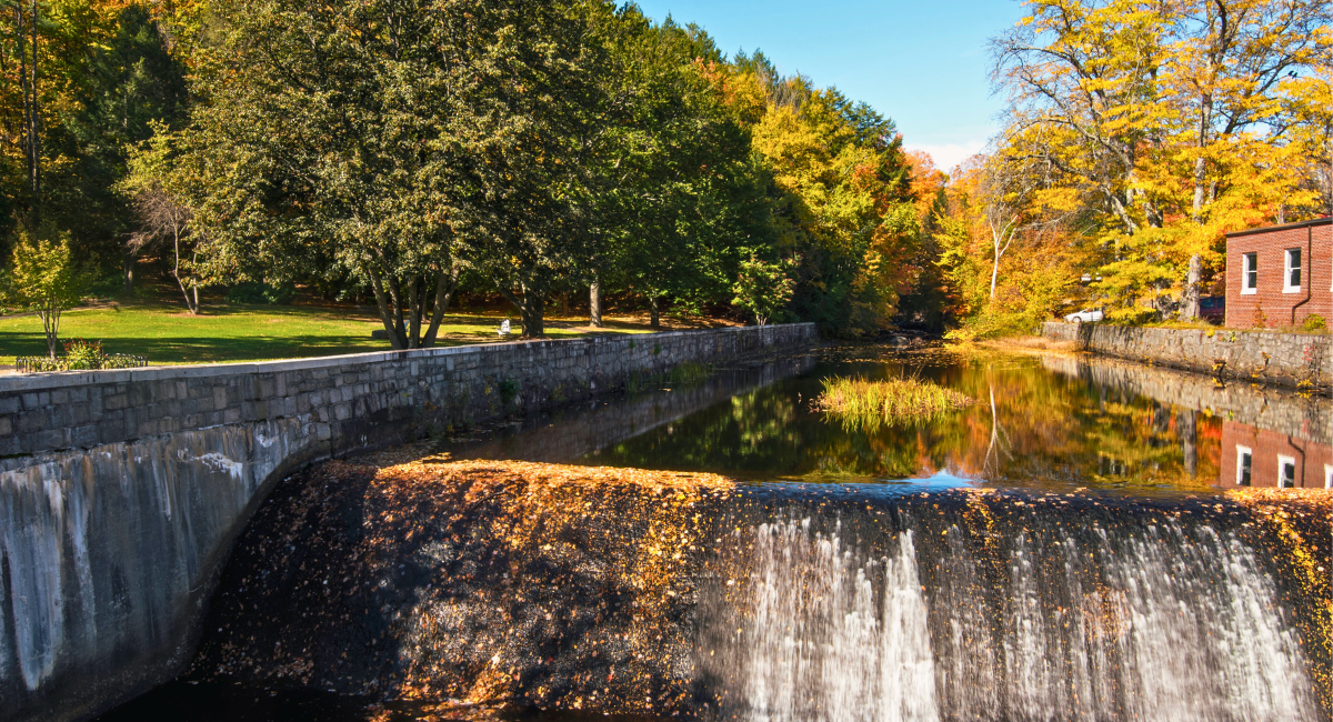 Scenic view of the dam in Putnam Park, Peterborough, with water flowing over the dam and reflecting the surrounding autumn trees