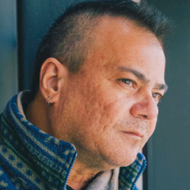 A thoughtful male patient gazing out of a window, wearing a blue and green patterned sweater.