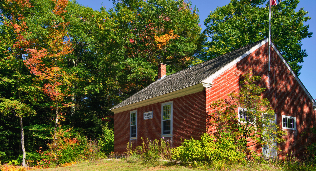 Charming snapshot of Sharon featuring one room schoolhouse and lush greenery under a bright blue sky