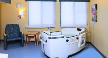 A color photograph of a birthing room featuring a birthing tub, comfortable chair, and medical equipment. The room is designed to provide a comfortable and soothing environment for childbirth, with soft lighting and modern amenities.