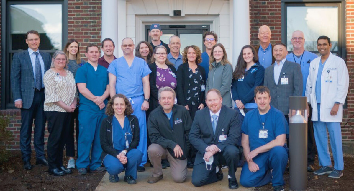 A large group of doctors, nurses, and staff members standing together outside of the Monadnock Community Hospital building.