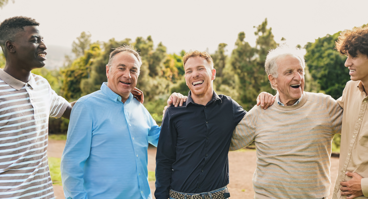 Diverse group of men standing outdoors with arms around each other, smiling and enjoying each other's company.