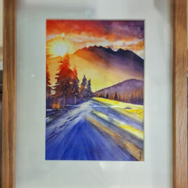 Framed watercolor painting of a scenic landscape with a winding road leading towards mountains under a dramatic sunset sky. The artwork captures the vibrant hues of the sunset, casting warm light over the scene