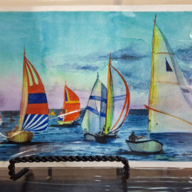 Watercolor painting of sailboats with colorful sails on a tranquil sea. The artwork features vivid reds, blues, and yellows against a soft blue sky, creating a lively nautical scene