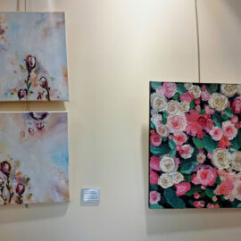 A display of three floral-themed paintings. The first two paintings are stacked vertically, showing pastel-toned abstract flowers. The third painting, titled "Roses," is rich with detailed, textured roses in shades of pink, white, and cream, set against a dark background that enhances the vividness of the blooms