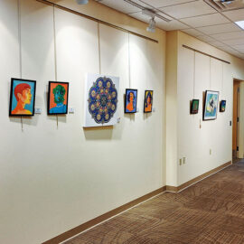 A brightly lit hallway at Monadnock Community Hospital displaying a diverse collection of framed artworks. The pieces, ranging from portraits to abstract designs, are evenly spaced along the wall, creating a visually engaging path through the hospital's corridors