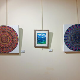 A trio of artworks at Monadnock Community Hospital, with the central piece being a watercolor painting of a mountainous landscape with a cloudy sky. On either side are two mandala designs, one in red and orange tones and the other in blue and purple hues