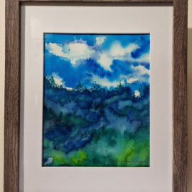 A framed watercolor painting titled 'Blue Hills' by Ann Marie Warren, featuring a landscape with rolling hills under a blue sky with fluffy clouds. The artwork is displayed with a simple gray frame