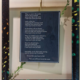 A framed poem titled 'Love Me Loud' by Jam Rizzi, displayed in a black frame with colorful painted accents. The poem expresses a heartfelt message about love, spanning from nature settings to familial gatherings, ending with a reflection on life's end.