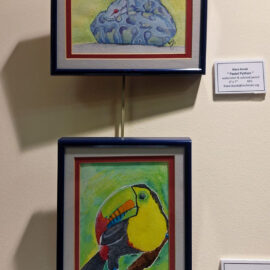 A set of two framed artworks by Kiera Burak, displayed vertically. The top painting, titled 'Pastel Python,' depicts a stylized python with colorful patterns. The bottom painting, titled 'Toucan,' features a vibrant toucan with a colorful beak against a green background