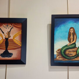 Two framed paintings of fantasy and elegance. On the left, a woman in a black dress poses dramatically on a grand staircase under a chandelier. On the right, a mermaid sits on a rock in the sea, surrounded by a mystical blue sky. The paintings are rich in detail and convey a sense of story and imagination