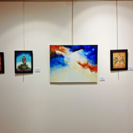 A gallery display featuring five paintings on a beige wall. From left to right, the paintings include a woman on a stage, a mermaid on a rock, a large abstract piece with vibrant blue and orange colors, and two paintings of elegantly dressed women