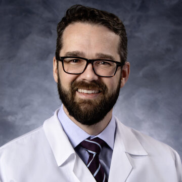 Dr. Robert Spencer, a cardiologist, smiling in his white medical coat and glasses, with a professional and welcoming demeanor