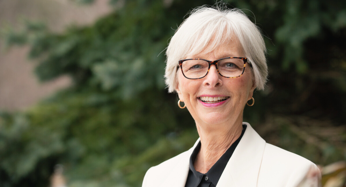 Cyndee McGuire, President and CEO of Monadnock Community Hospital, stands smiling in a brightly lit office, wearing a professional outfit with a welcoming demeanor.