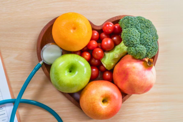 A heart shaped bowl with healthy fruit and vegetables inside and a stethoscope on the side