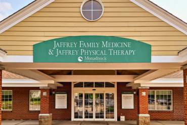 The entrance to Jaffrey Family Medicine & Jaffrey Physical Therapy features a wide green awning with the practice's name and the Monadnock Community Hospital logo. The brick building has large glass doors and a welcoming appearance