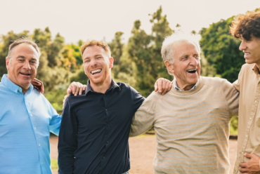 A group of smiling men from multiple generations outside on a sunny day