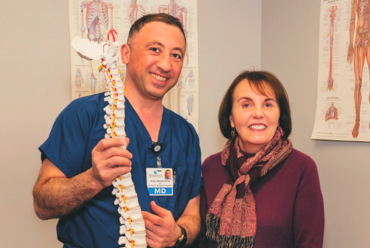 Dr Vache holds up a model of a spine while a smiling patient stands next to him