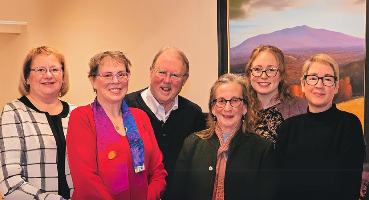 Members of the Patient & Family Advisory Council at Monadnock Community Hospital. From left to right: Denise Lord, VP of Organizational Performance; Vicky Rank; John Richards; Judy Unger-Clark; Molly Rajaniemi, Patient Experience Coordinator; and Lisa McInnis, MHP Practice Liaison. The group stands in front of a landscape painting, smiling, and showcasing their commitment to improving patient care and community engagement.